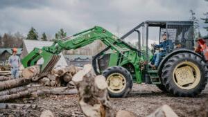 Student operating an earth mover to transport logs